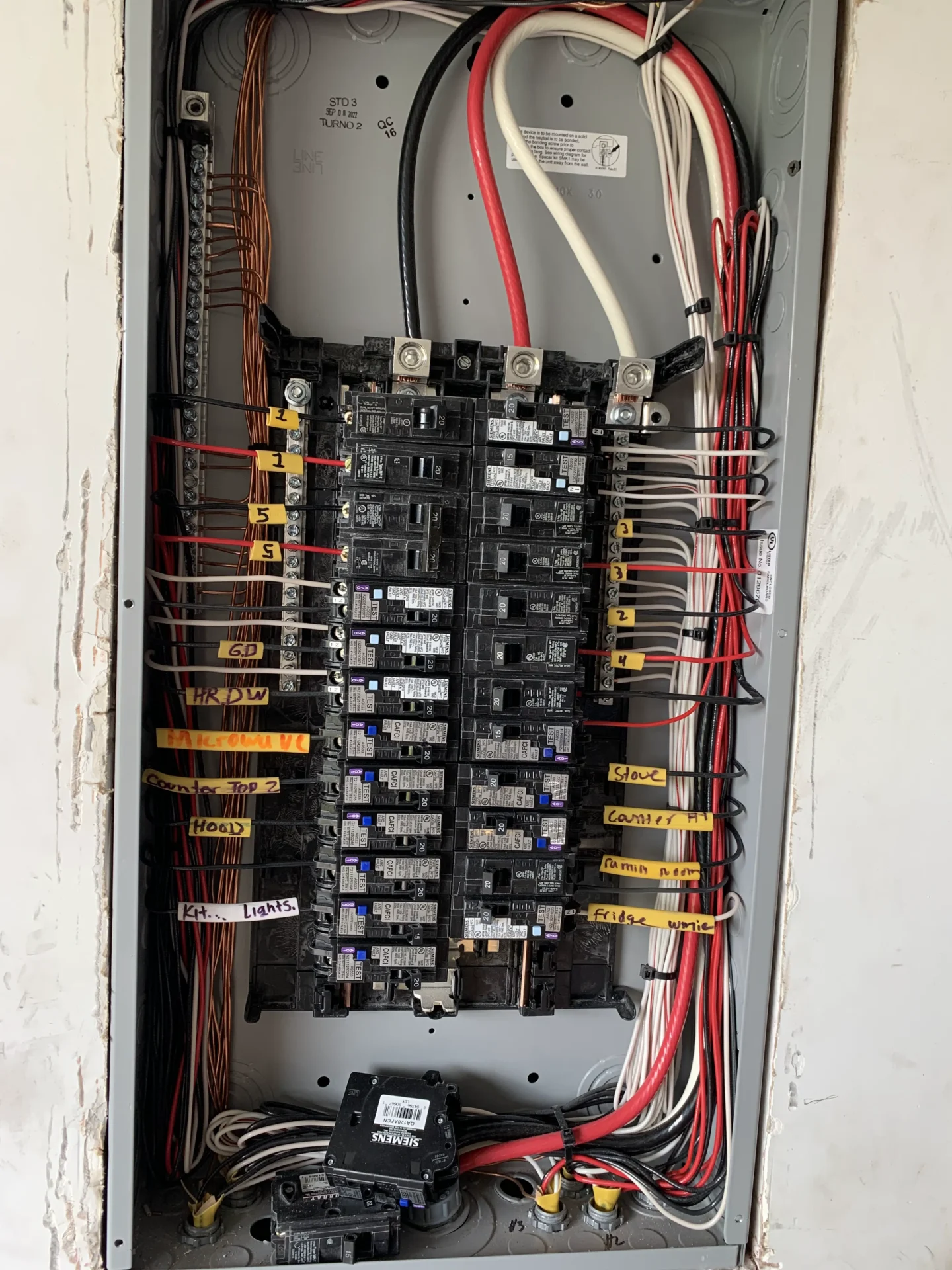 An open electrical panel with multiple circuit breakers, wires organized and labeled with yellow tags, showing detailed internal wiring and connections.