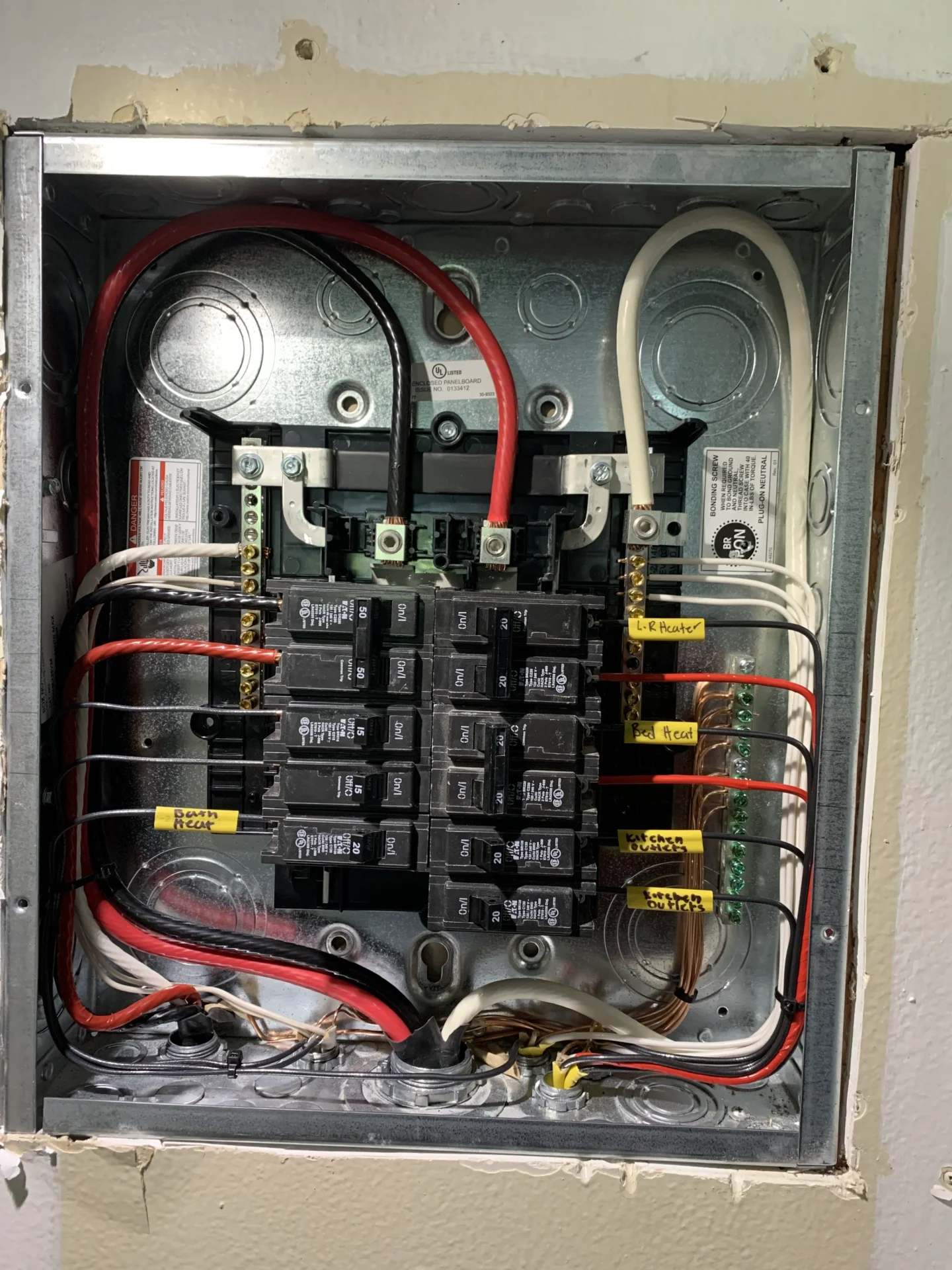 Close-up of an electrical breaker panel with labeled wires and circuit breakers, showing detailed internal wiring and connections.